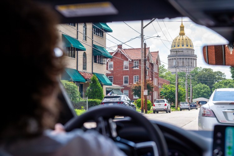 A building with a gold domed roof can be seen through the windshield of a car. The driver is a woman with brown hair and a white shirt.