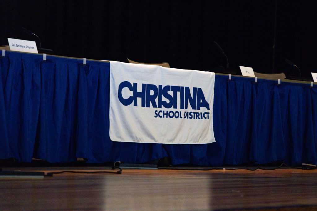 A Christina School District banner sits at the table reserved for school board members during a public meeting in July 2025.