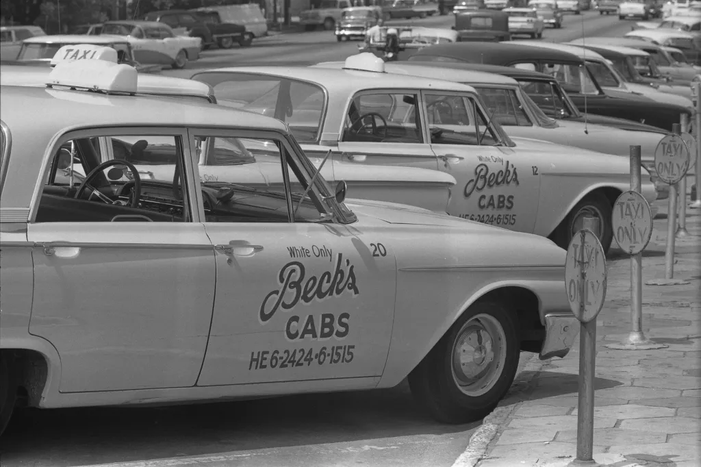 A line of parked cabs with writing on their doors that says “White Only Beck’s Cabs” with a phone number.