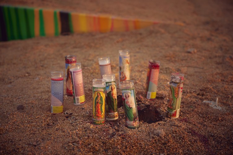 A grouping of ten slender prayer candles in sand.