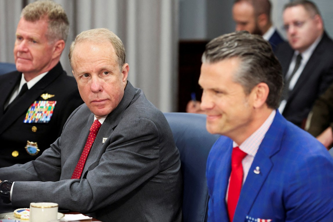 Three men sitting at a table. Feinberg and Hegseth are in suits while the third is in military dress uniform.