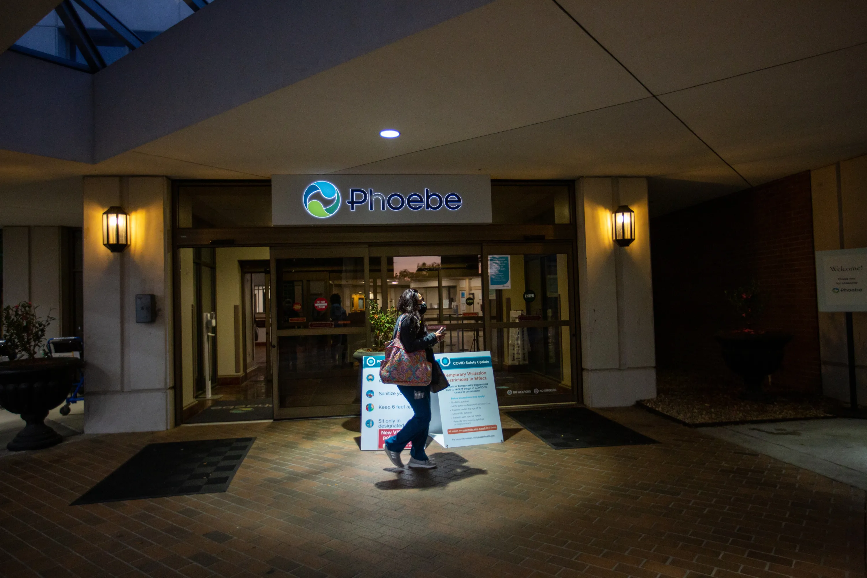 At the entrance of Phoebe Putney Memorial Hospital, a harsh spotlight shines on a woman walking across the frame.