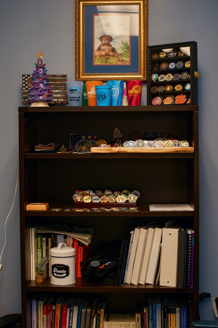 A bookcase full of knickknacks, cups, binders and pins.