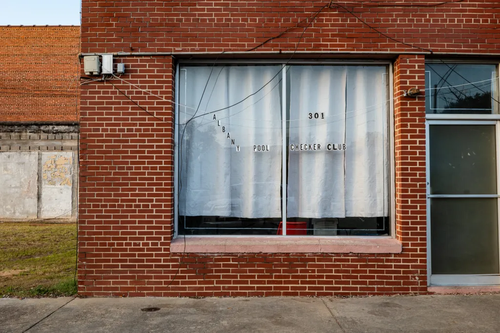 The facade of a brick building. Stickers in the window read “Albany Pool Checker Club.”