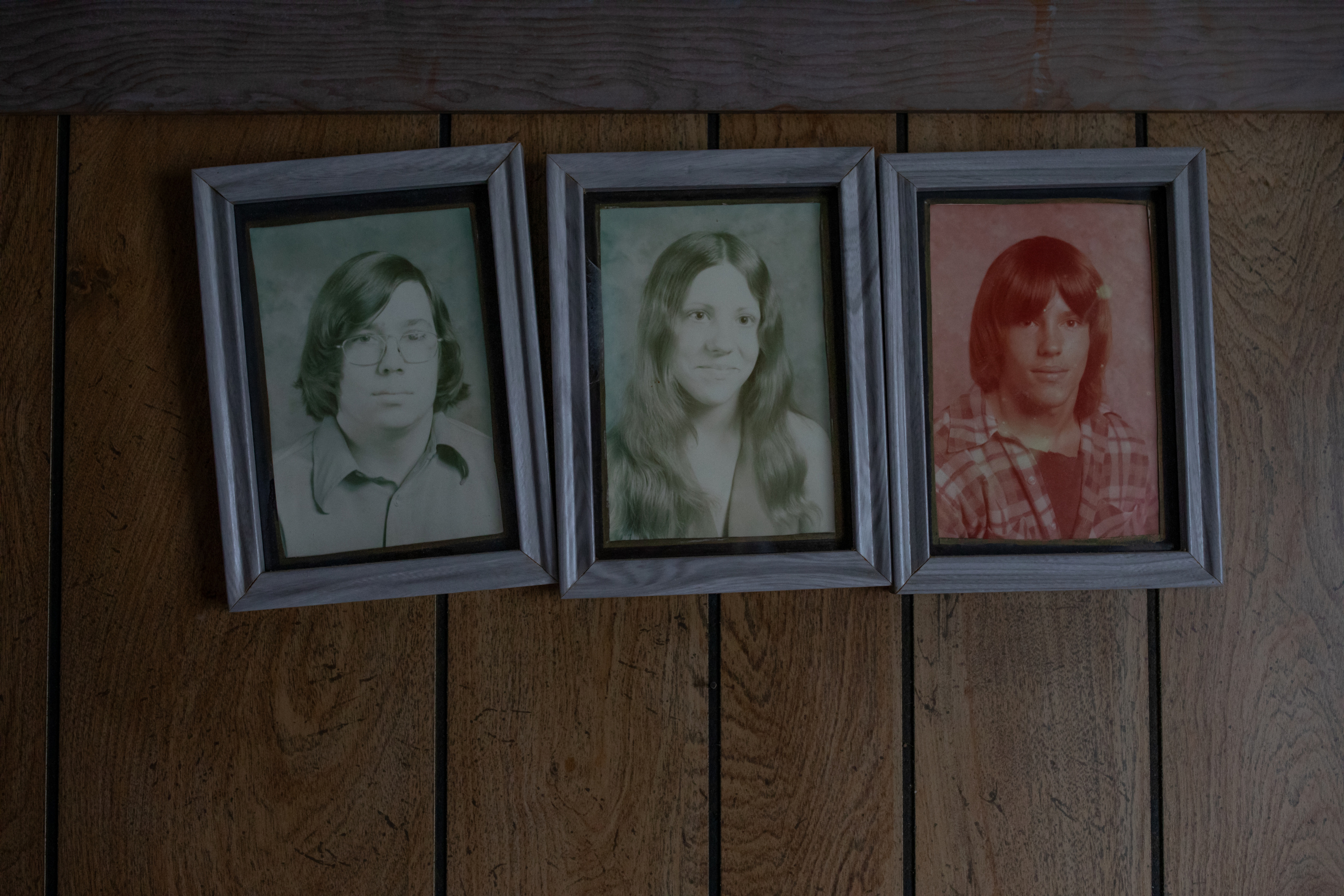 Three framed archival photos of young people hang slightly askew on a wooden wall.
