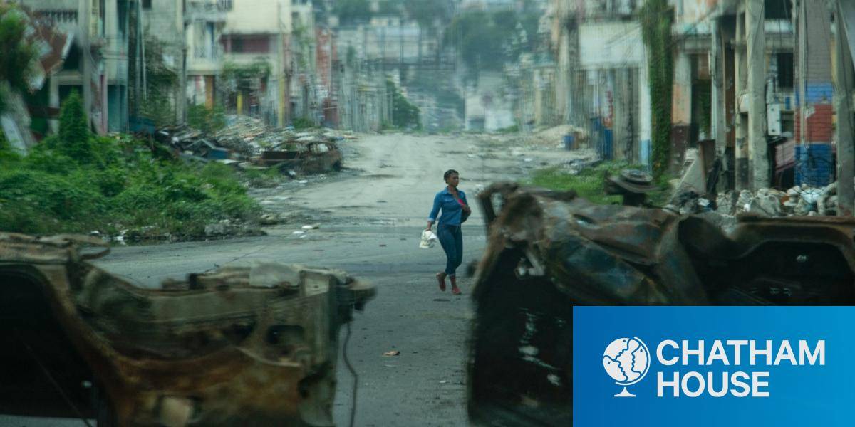 A Haitian walks past cars burned by armed gangs and used as a barricade during clashes with security forces