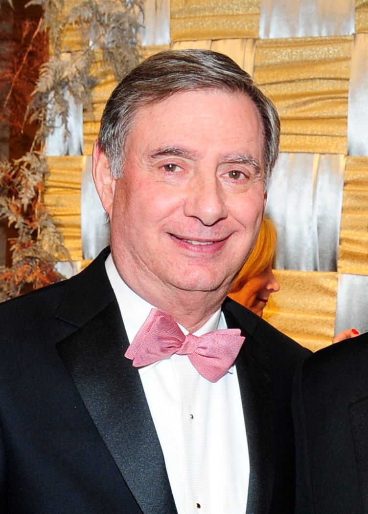 A man with short greying hair, wearing a tuxedo and a pink bowtie.
