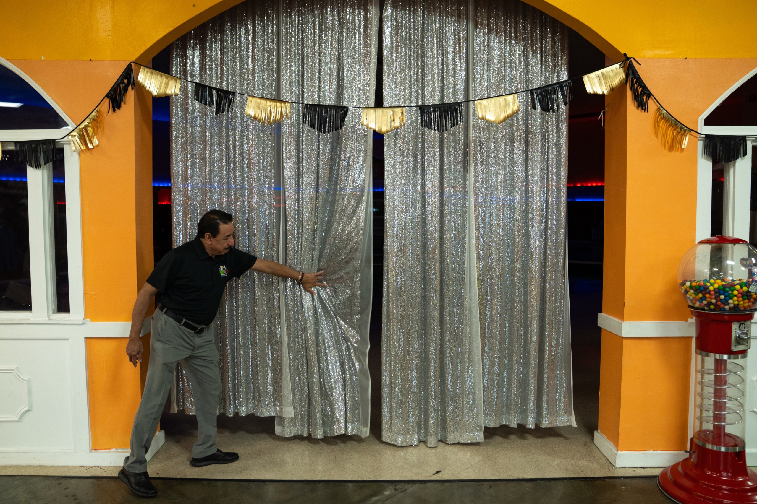A man reaches for a silvery curtain hanging between two bright orange columns.